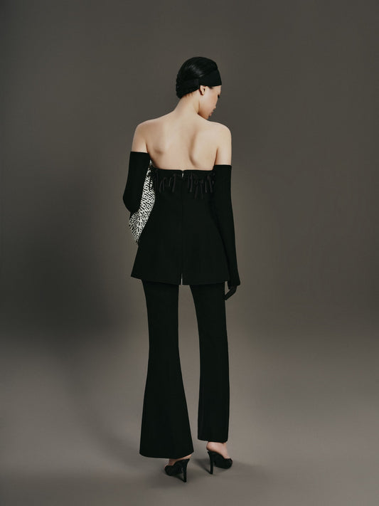 Woman wearing a black off-shoulder top and flared pants against a gray background