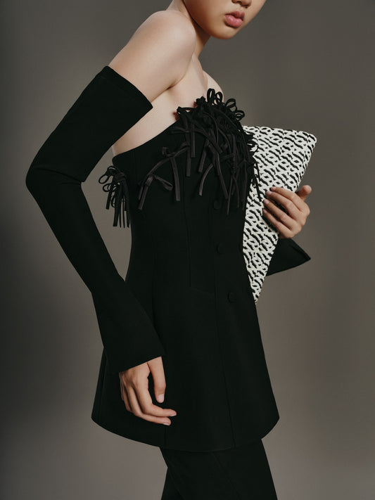 Woman wearing a black off-shoulder outfit holding a patterned clutch against a gray background