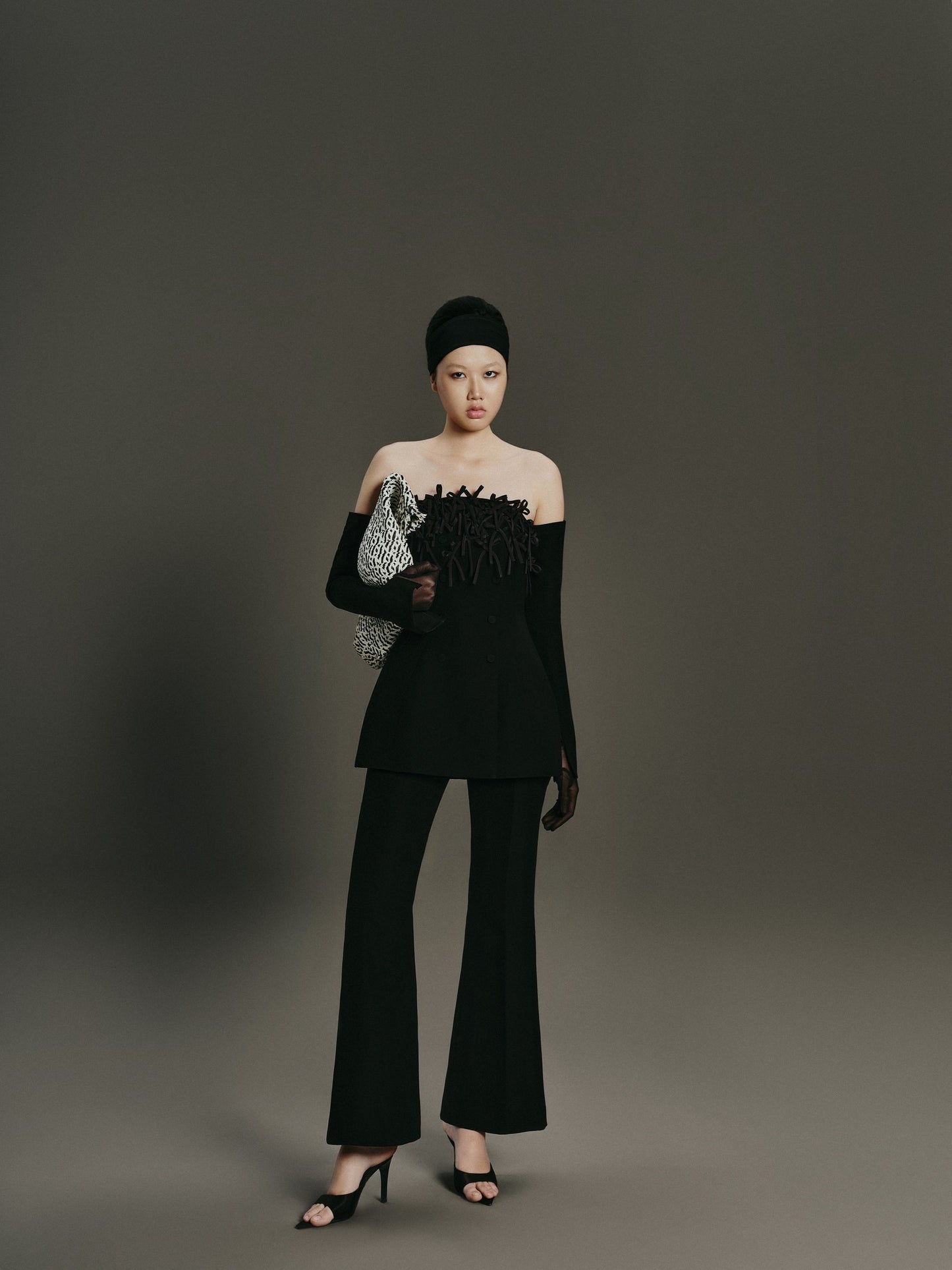 Woman in a black outfit holding a clutch against a gray background