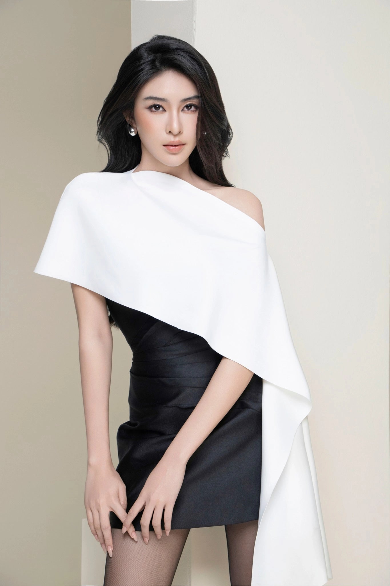 Woman wearing a black dress with a white cape over a beige background