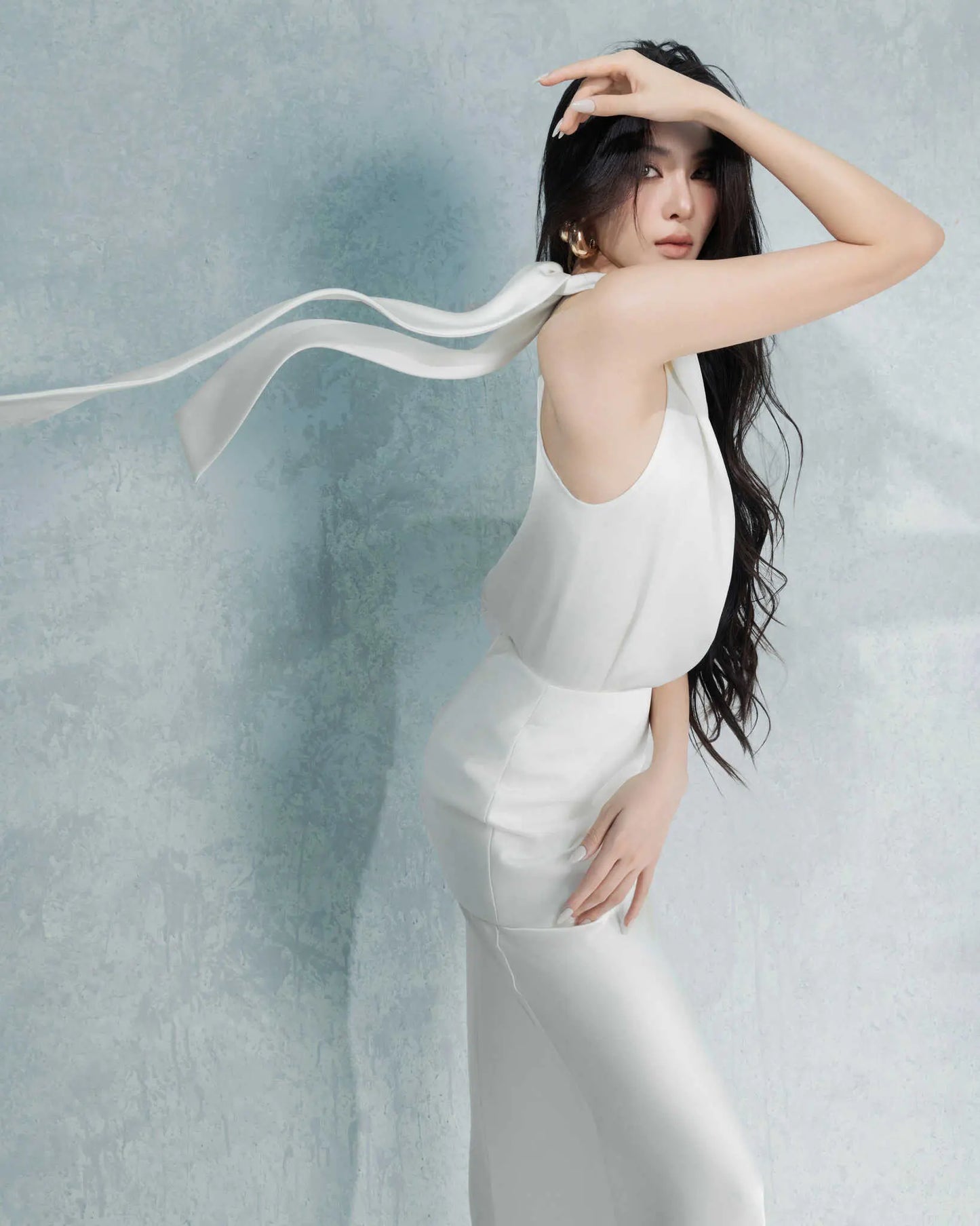 Woman in a white dress with a flowing ribbon against a light blue background