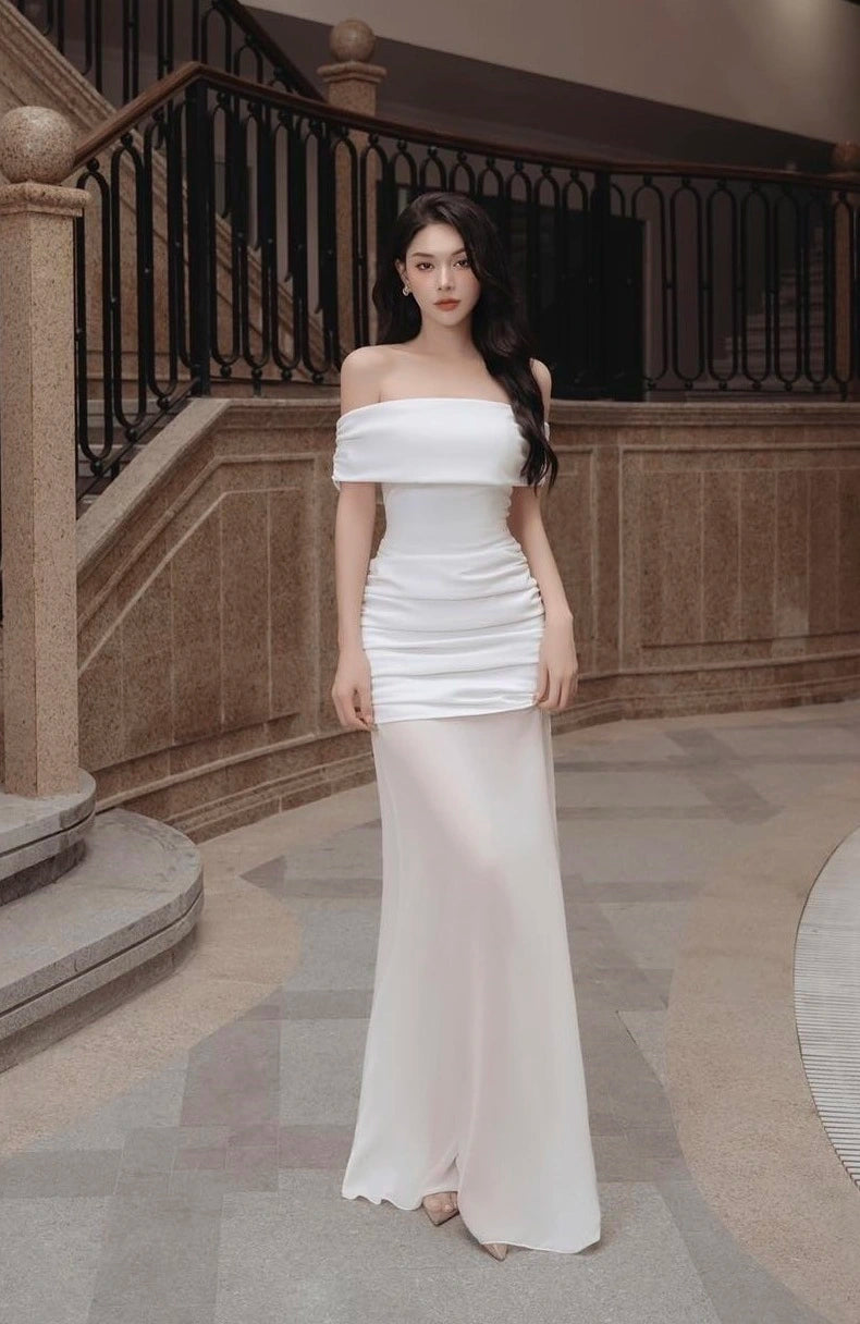 Woman in a white off-shoulder gown standing in an elegant interior setting.