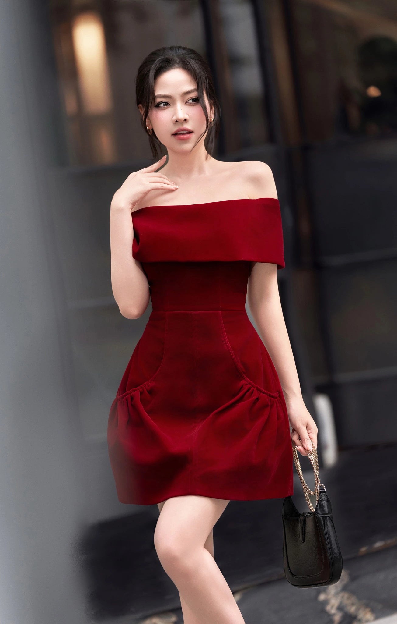 Woman wearing a red off-shoulder dress holding a black handbag against a blurred background