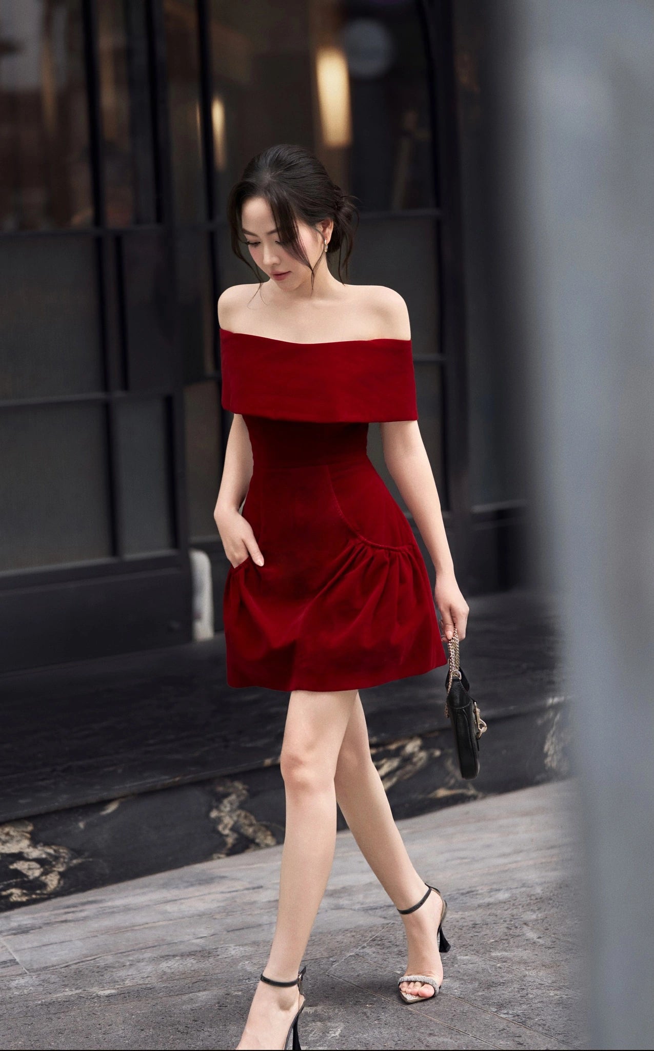 Woman wearing a red off-shoulder dress walking outdoors.