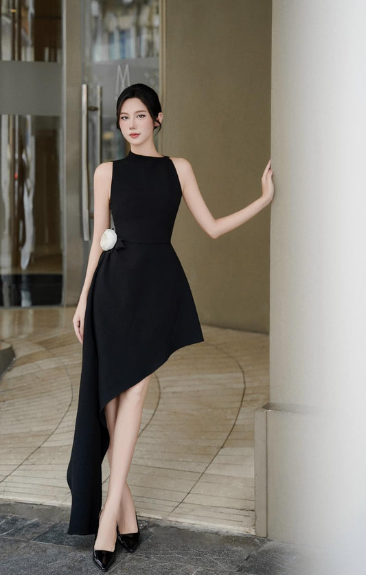 Woman in a black dress standing against a modern building entrance.