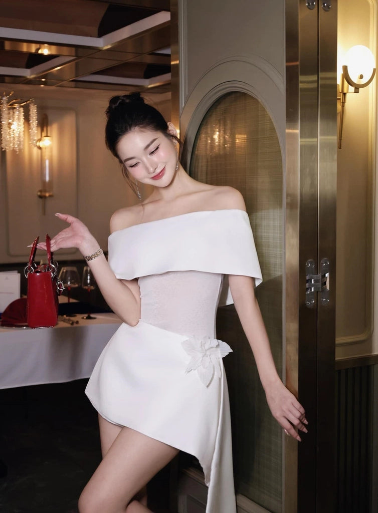 Woman in a white off-shoulder dress standing in an elegant interior setting.