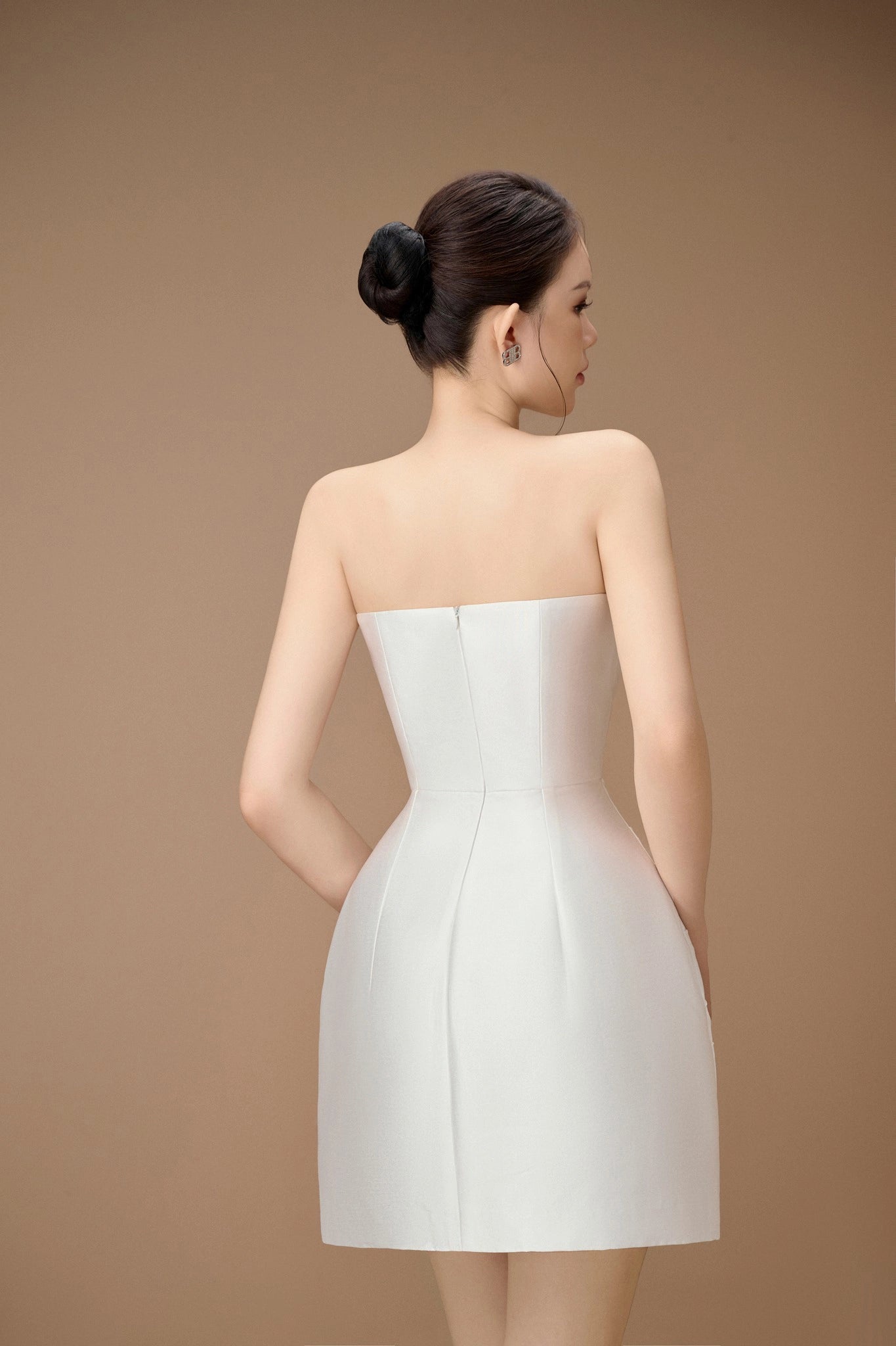 Woman wearing a strapless white dress against a beige background