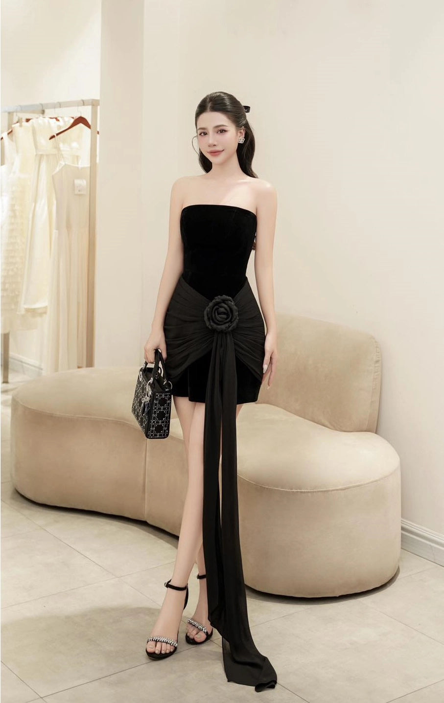 Woman in a black strapless dress with a large floral detail in a room with beige furniture.
