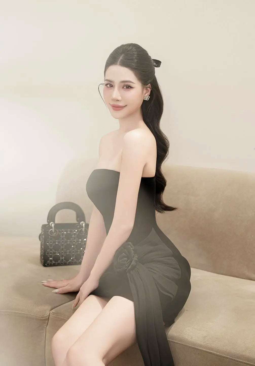 Woman in a black dress sitting on a beige couch with a handbag beside her.