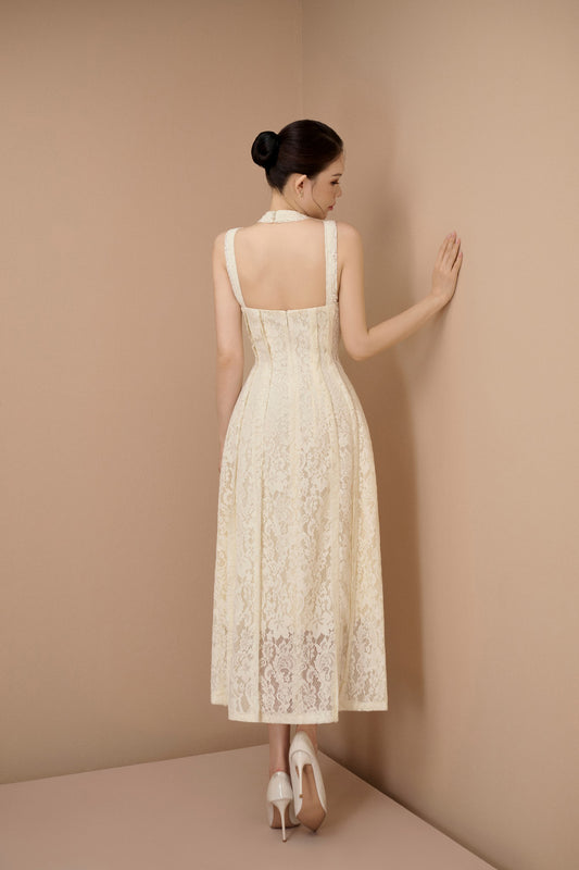 Woman in a white lace dress standing against a beige wall.