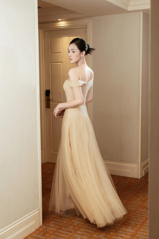 Woman in a beige evening gown standing in a doorway.