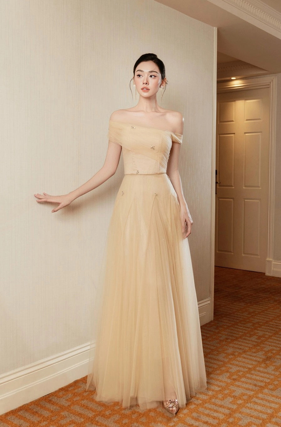 Woman in a beige strapless gown standing in an elegant room.