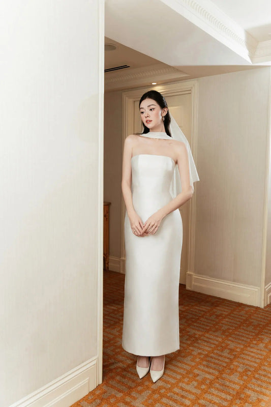 Woman in a white wedding dress standing in a doorway with a neutral background
