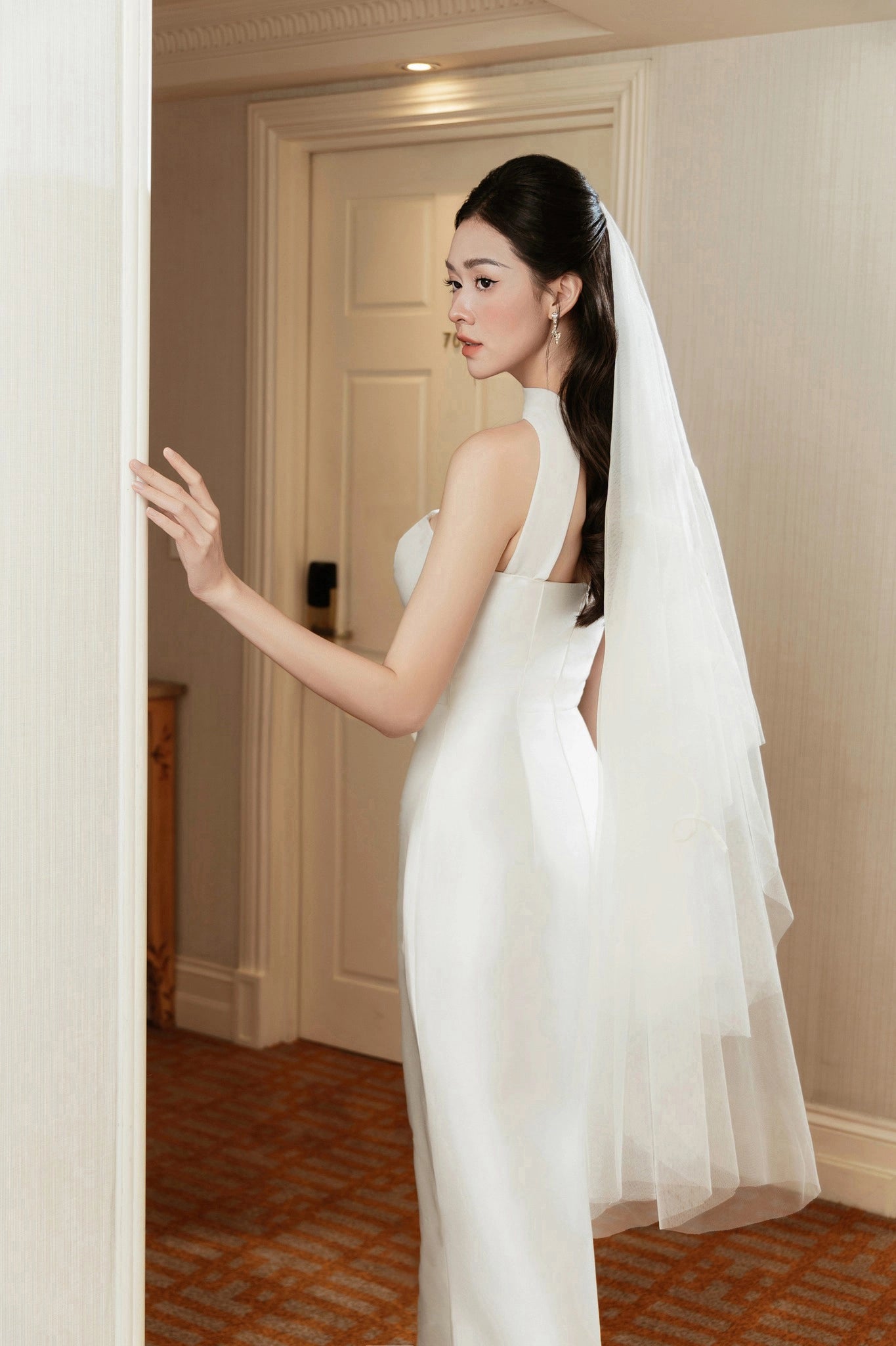Woman in a white wedding dress with a veil standing in a doorway.
