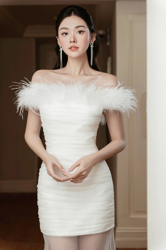 Woman wearing a white off-shoulder dress with feather details in an indoor setting