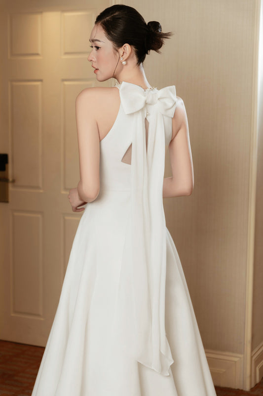 Woman wearing a white dress with a large bow detail in a room.