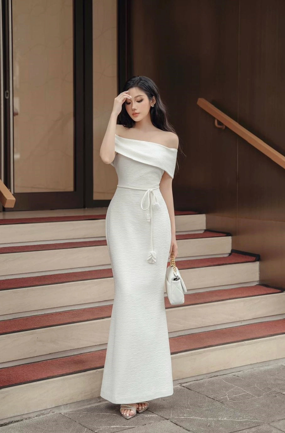 Woman in a white off-shoulder dress standing on steps