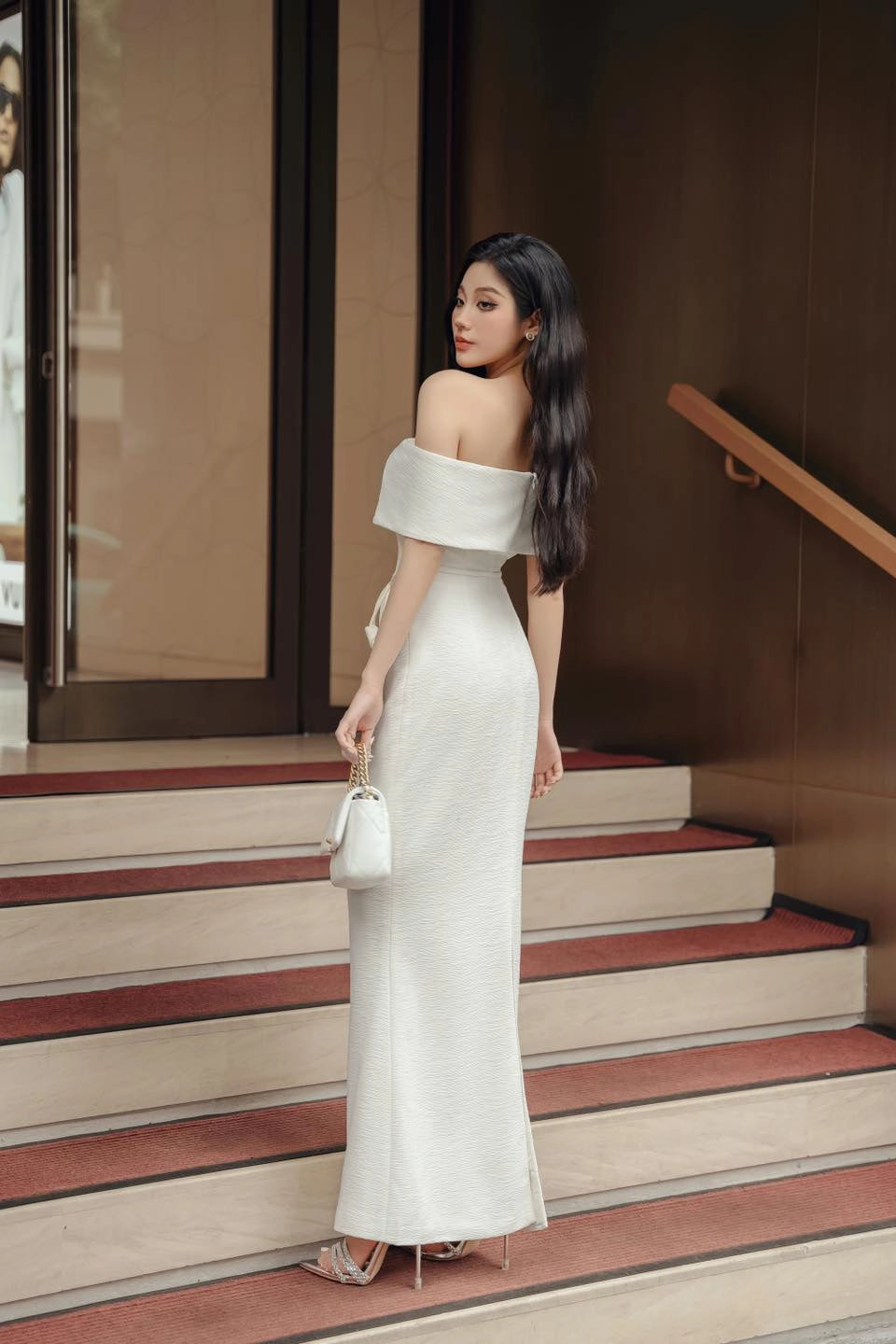 Woman in a white off-shoulder dress standing on steps