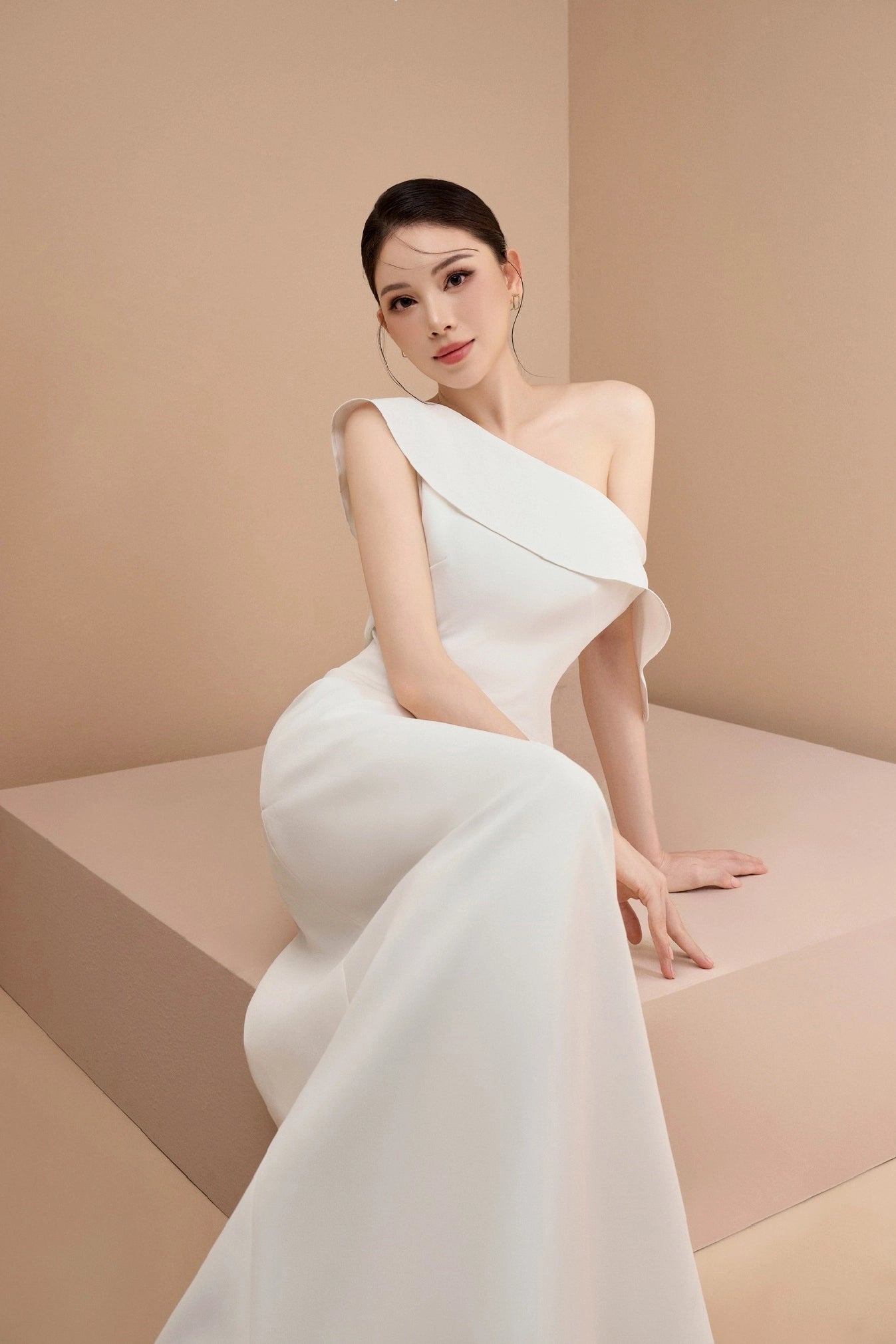 Woman in a white one-shoulder dress against a beige background