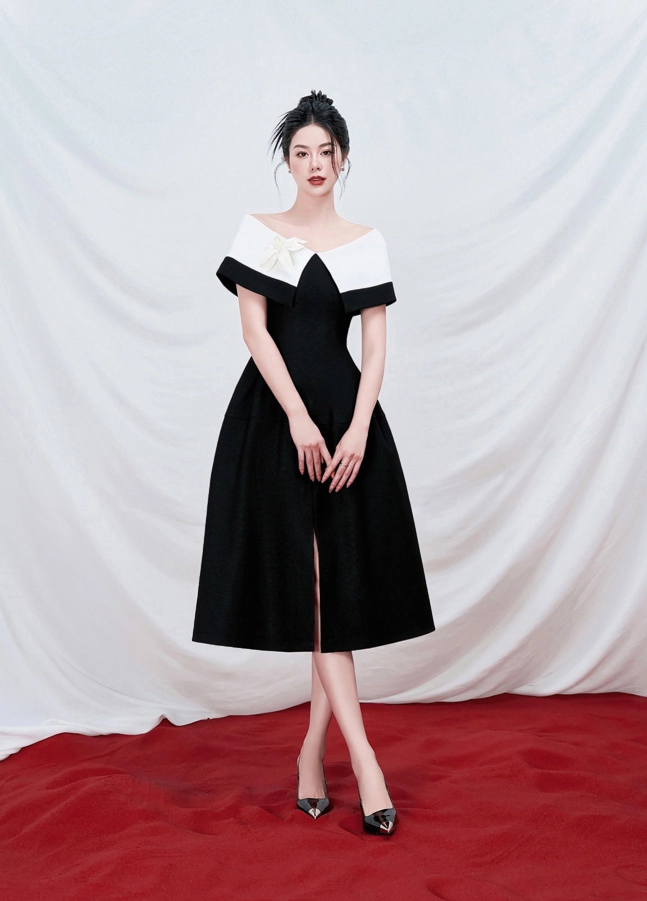 Woman in a black and white dress standing on a red carpet with a white curtain background