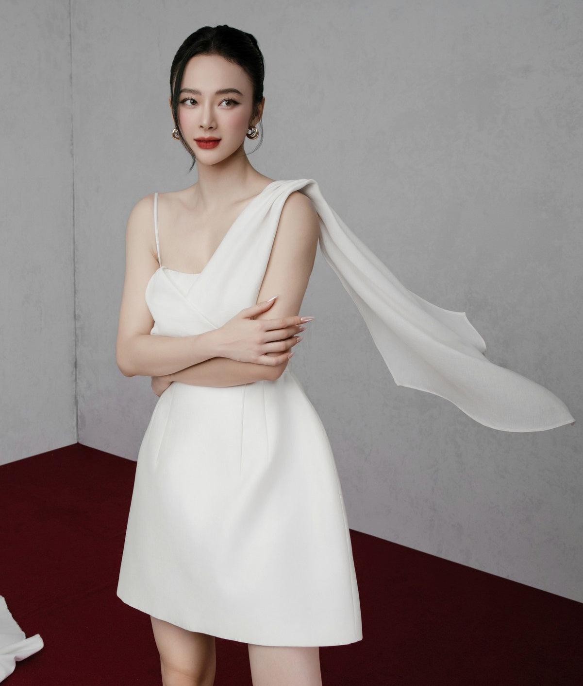 Woman in a white dress with a sheer overlay against a plain background