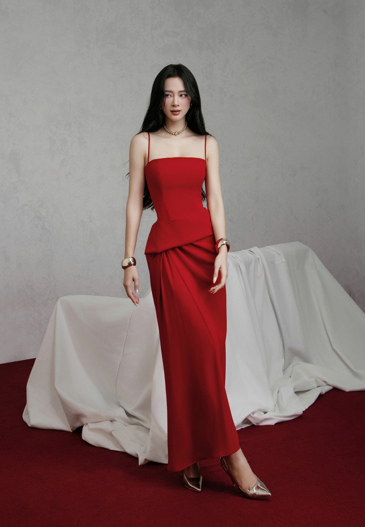 Woman in a red dress standing against a gray background with draped fabric.