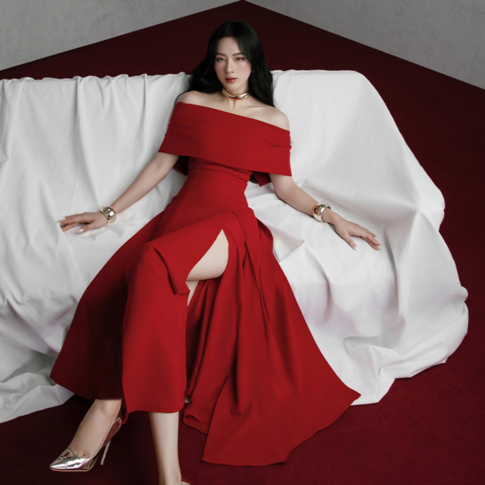 Woman in a red off-shoulder dress sitting on a white draped fabric.