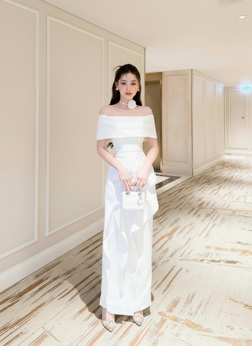 Woman in a white off-shoulder dress standing in an elegant indoor setting.