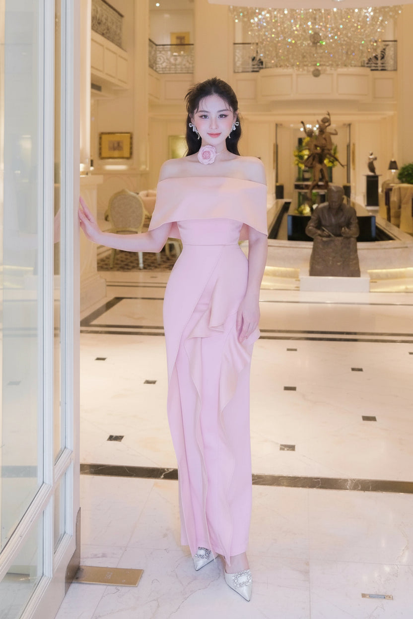 Woman in a pink off-shoulder dress standing in a stylish interior setting.