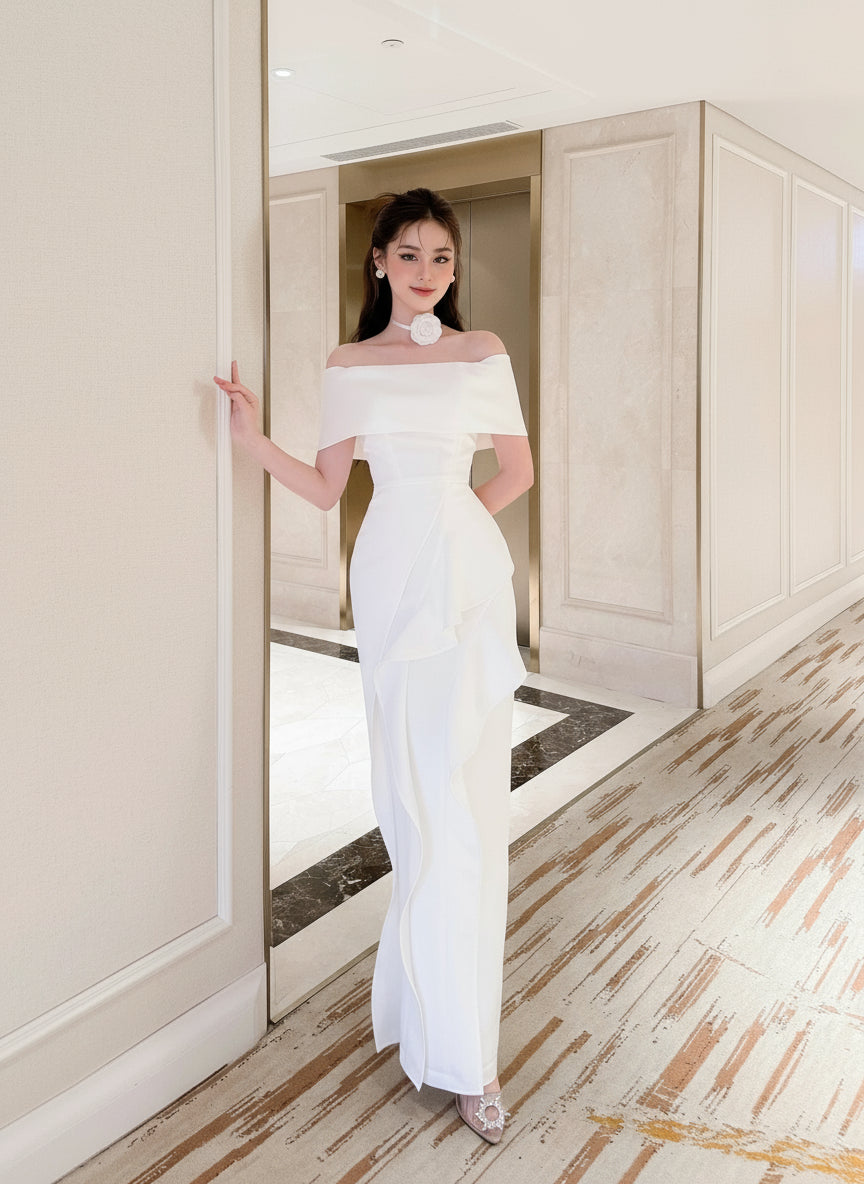 Woman in a white off-shoulder gown standing in a hallway.