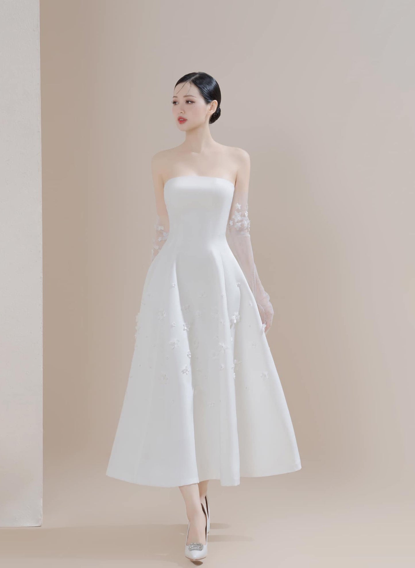 Woman wearing a white strapless dress with sheer sleeves against a beige background