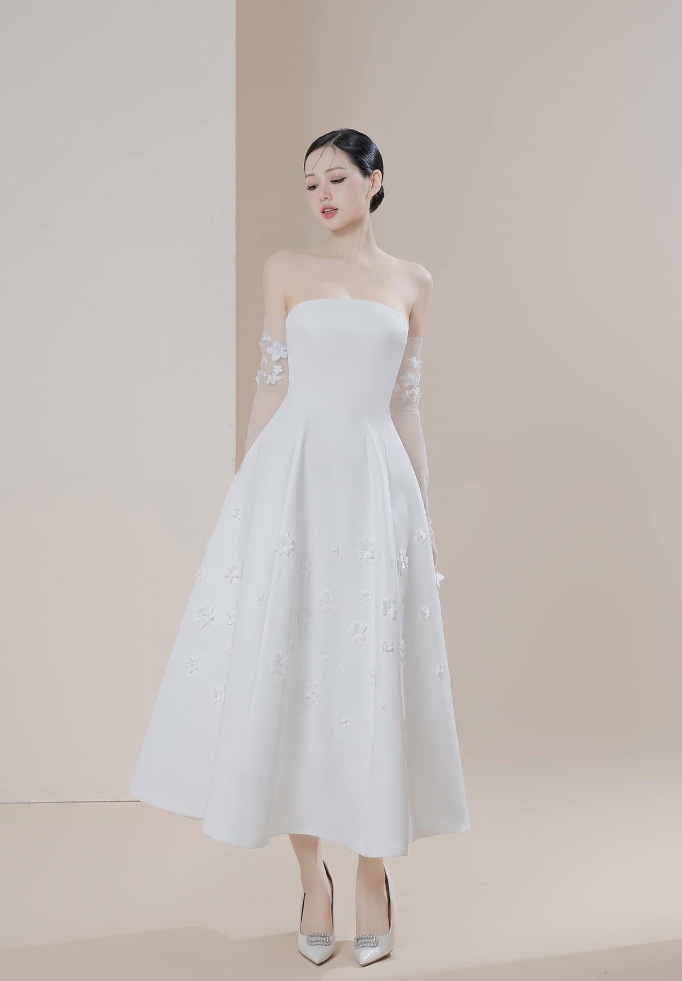 Woman wearing a strapless white dress with floral details against a beige background