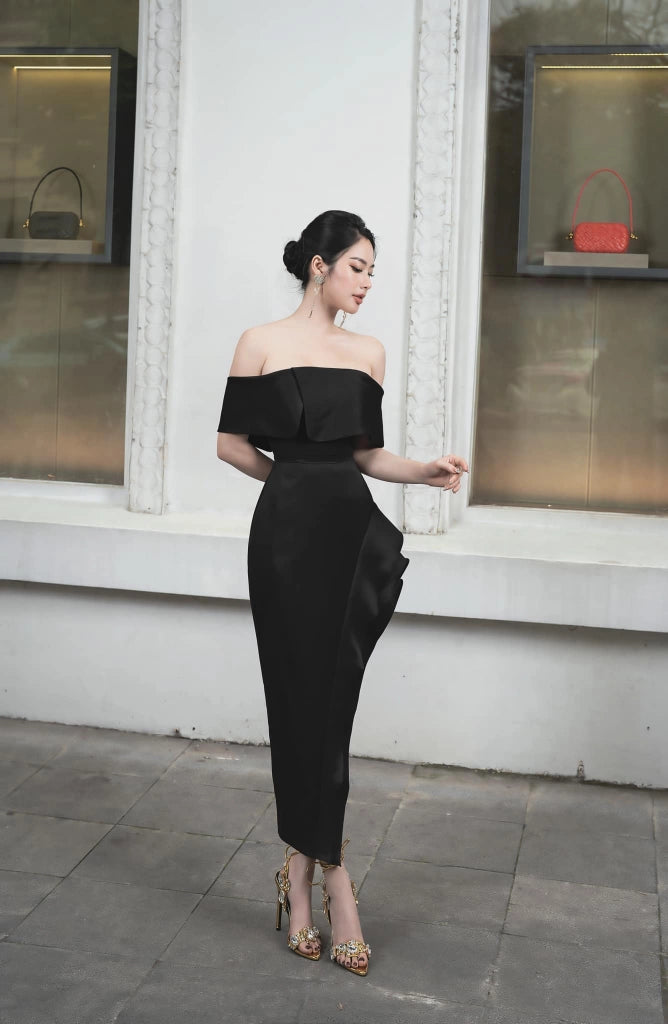 Woman in a black off-shoulder dress standing in front of a store window.
