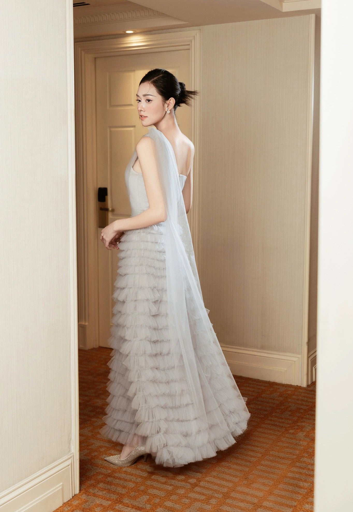 Woman in a elegant white dress with ruffled layers standing in a doorway.