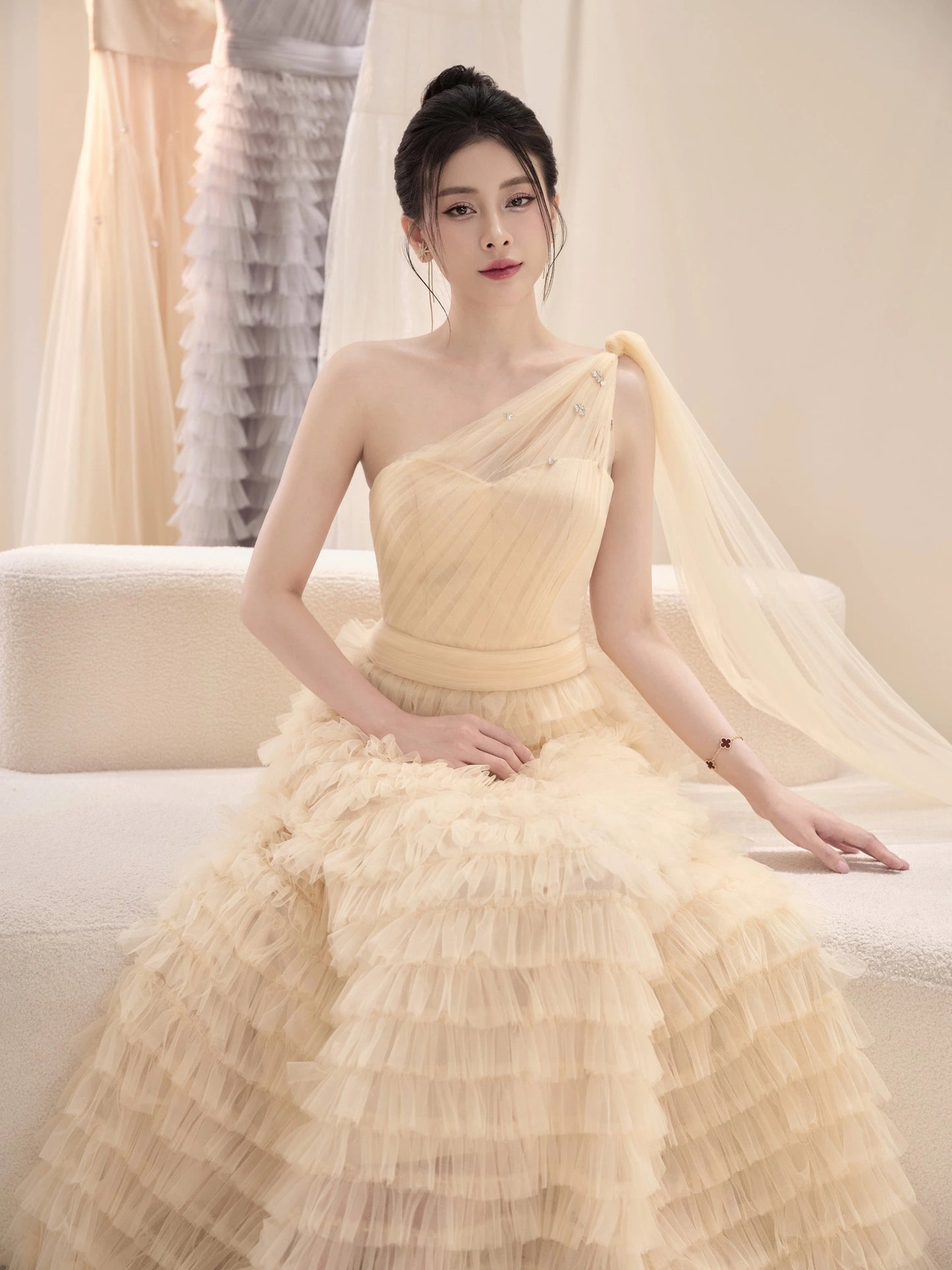 Woman in a light yellow one-shoulder dress sitting on a white couch.