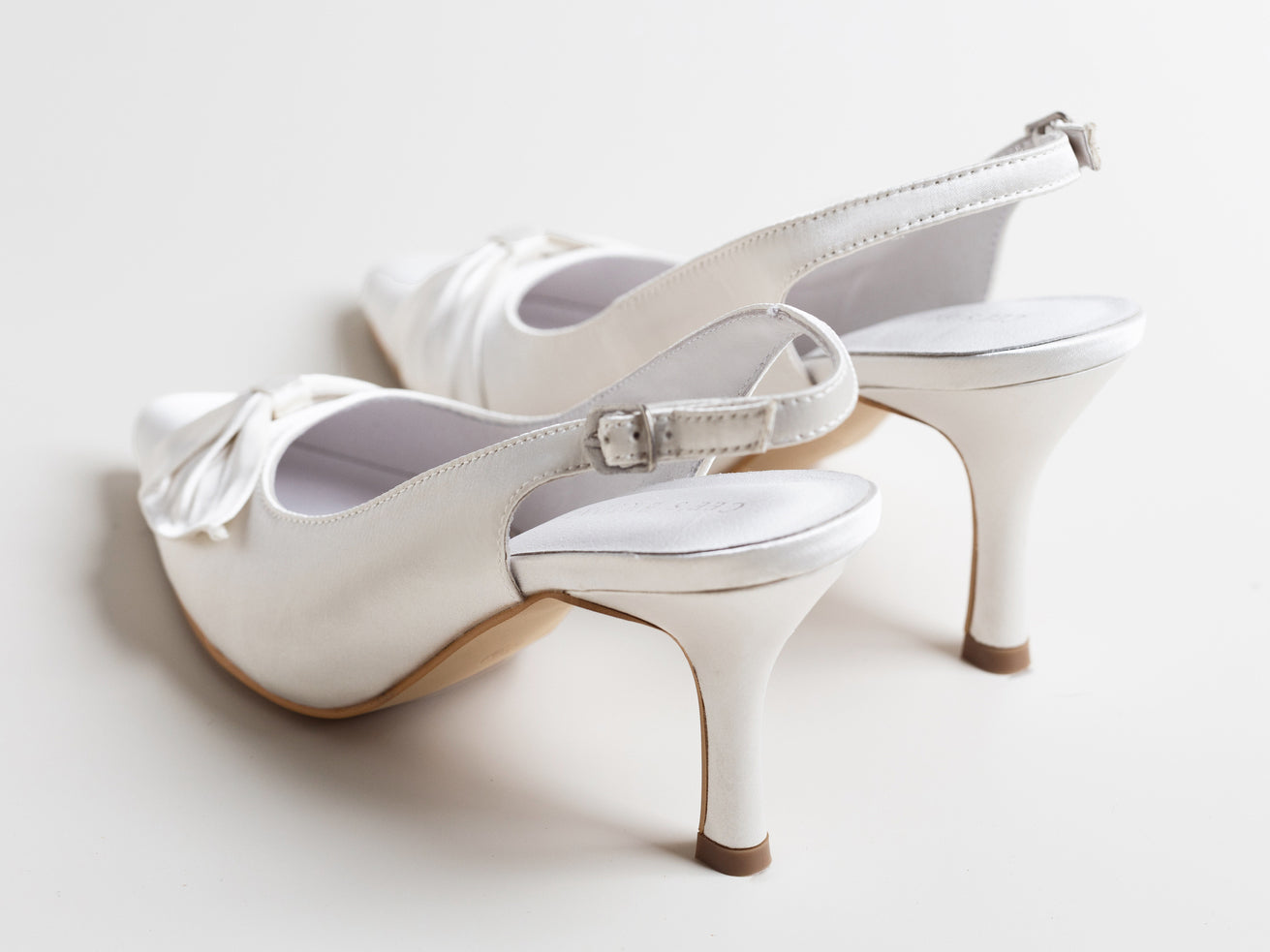 White high-heeled shoes with bow details on a light background