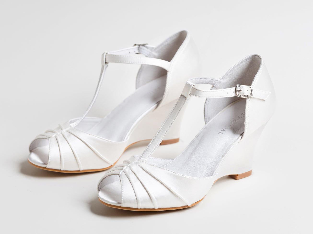 Pair of white wedding shoes with open toes and thin straps on a light gray background