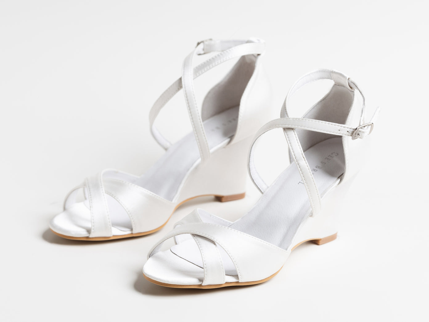White high-heeled sandals with thin straps on a light gray background