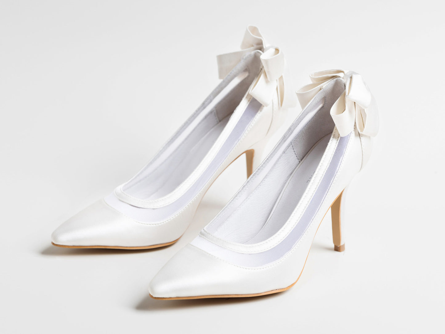 White high-heeled shoes with bow details on a light gray background