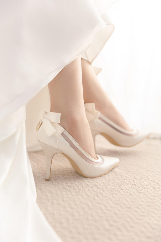 White high-heeled shoes with bow details on a light background
