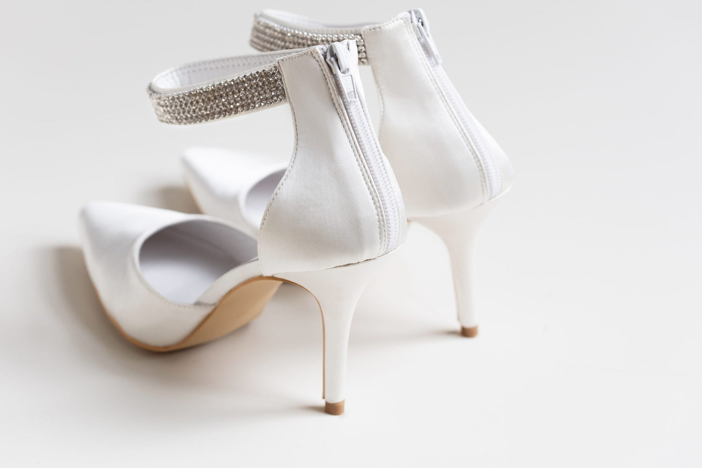White high-heeled shoes with embellished straps on a light background