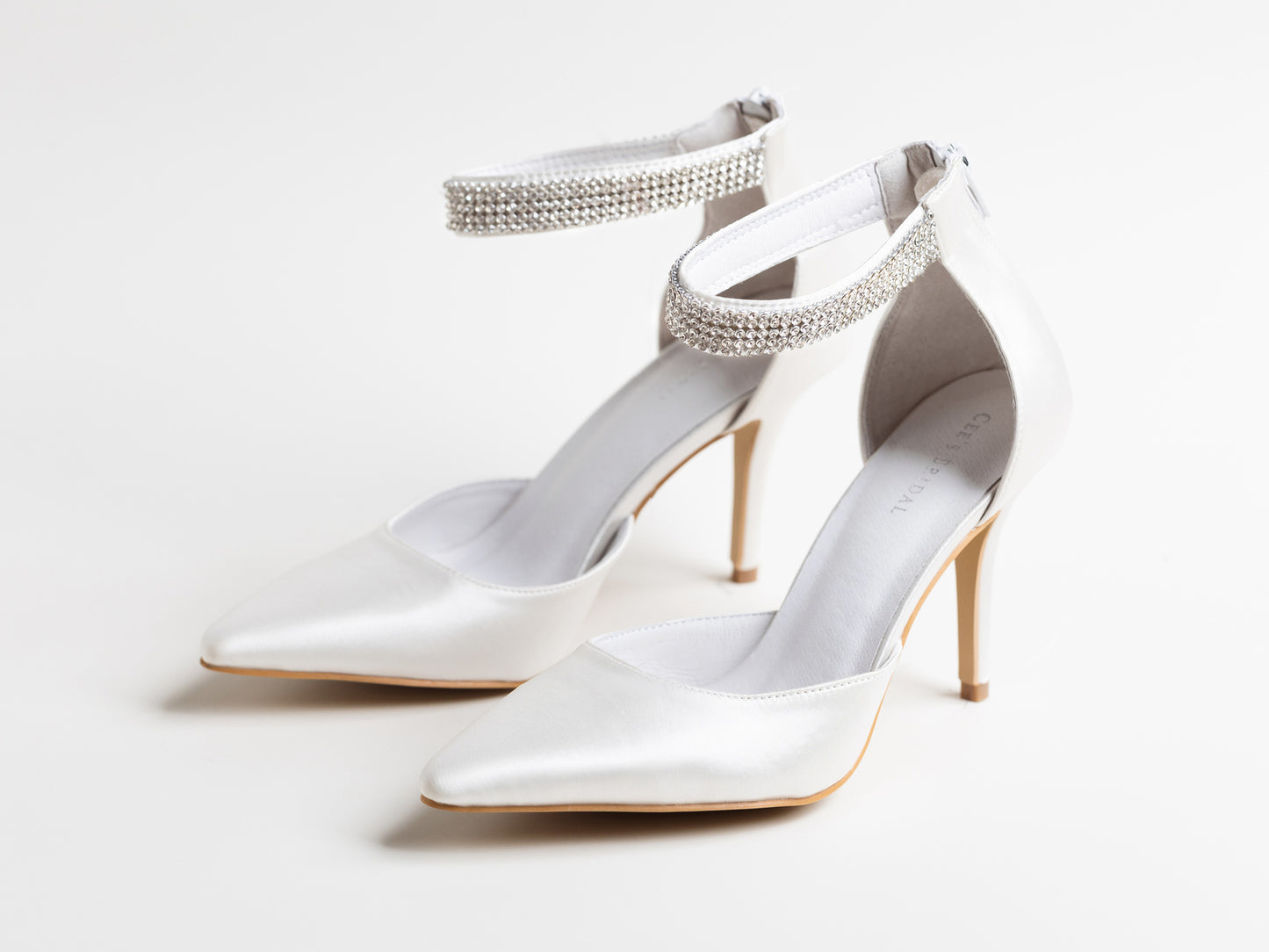 White high-heeled shoes with embellished straps on a light gray background