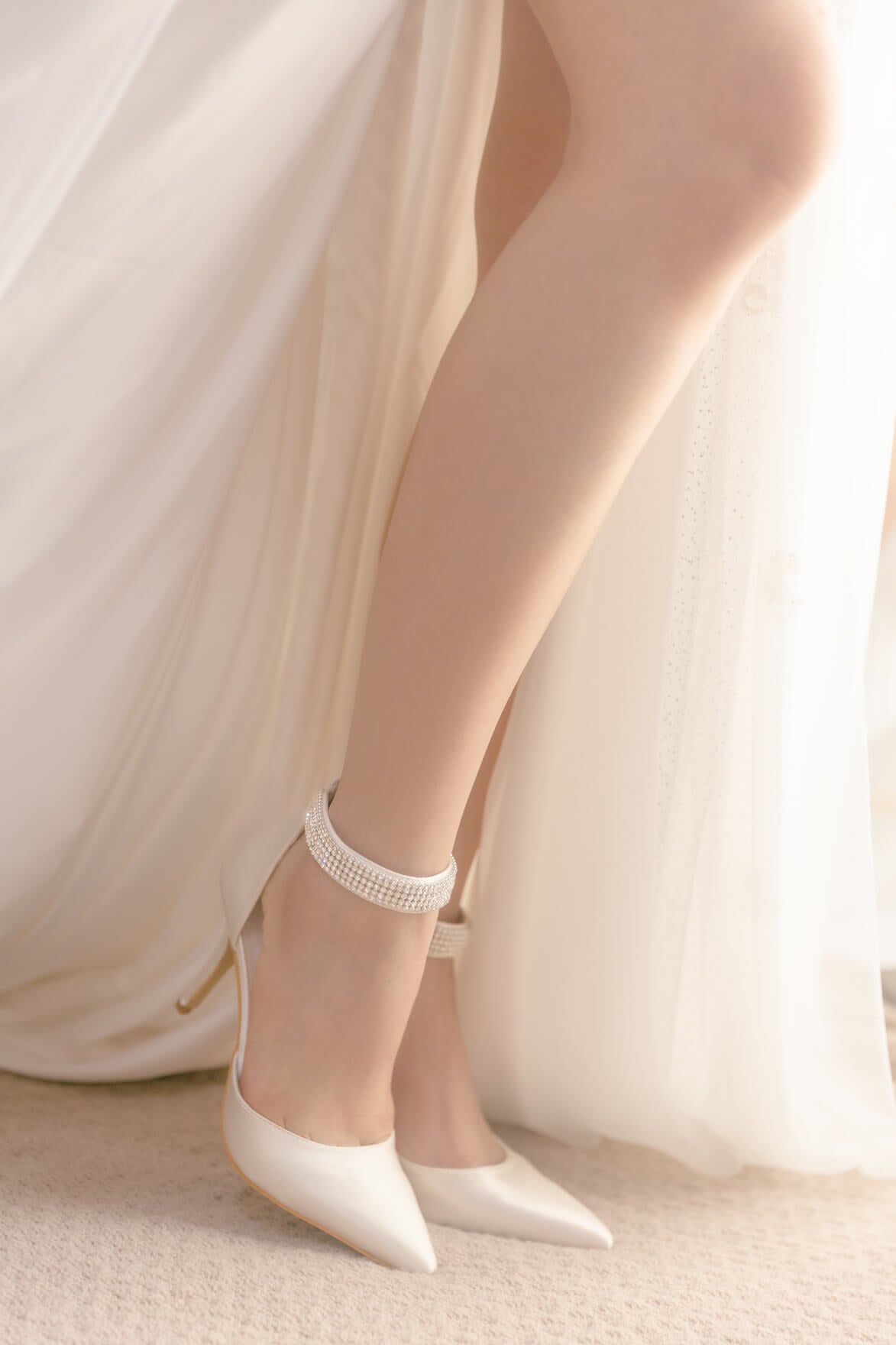 White high-heeled shoes with a decorative anklet on a neutral background