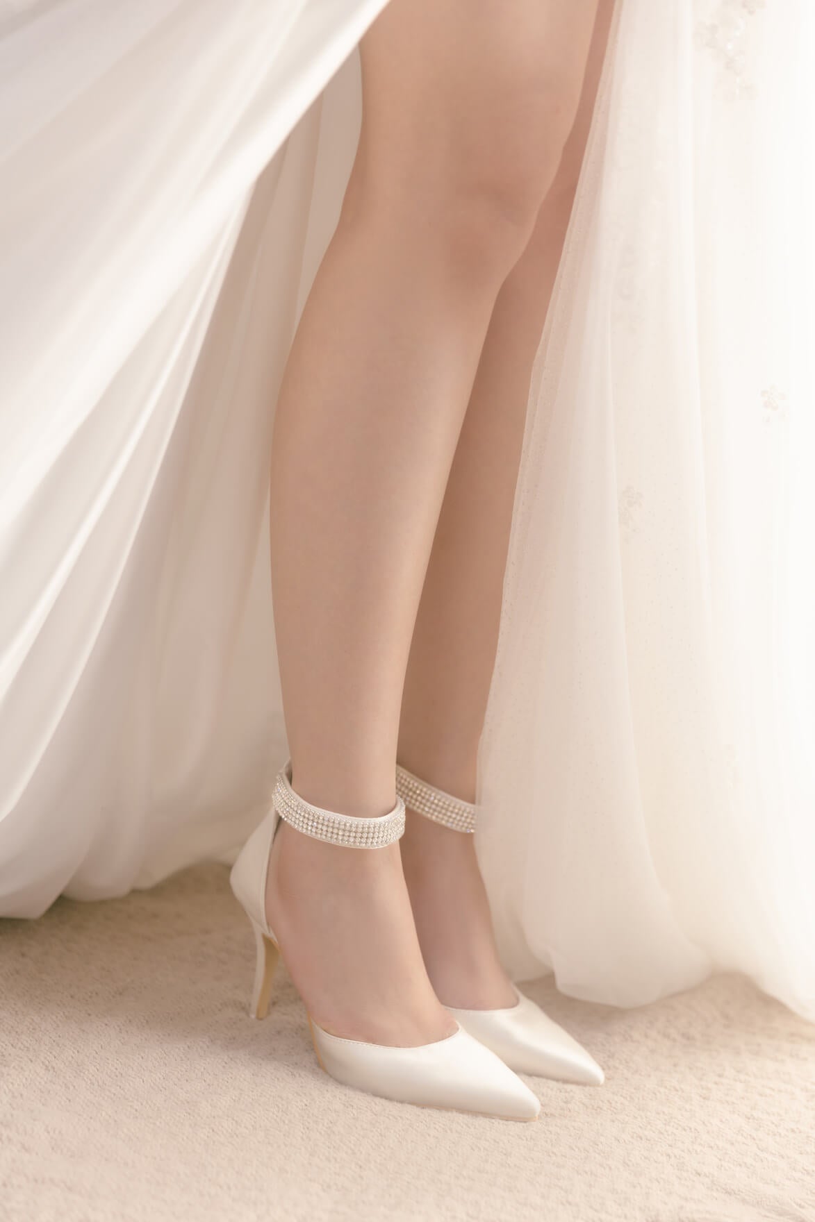White high-heeled shoes with lace details worn by a person in a white dress.