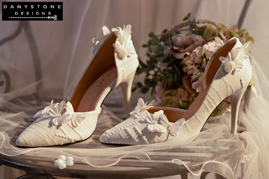 White lace wedding shoes with butterfly decor and 9cm heels, placed on a lacy fabric surface with sunlight highlighting the details.