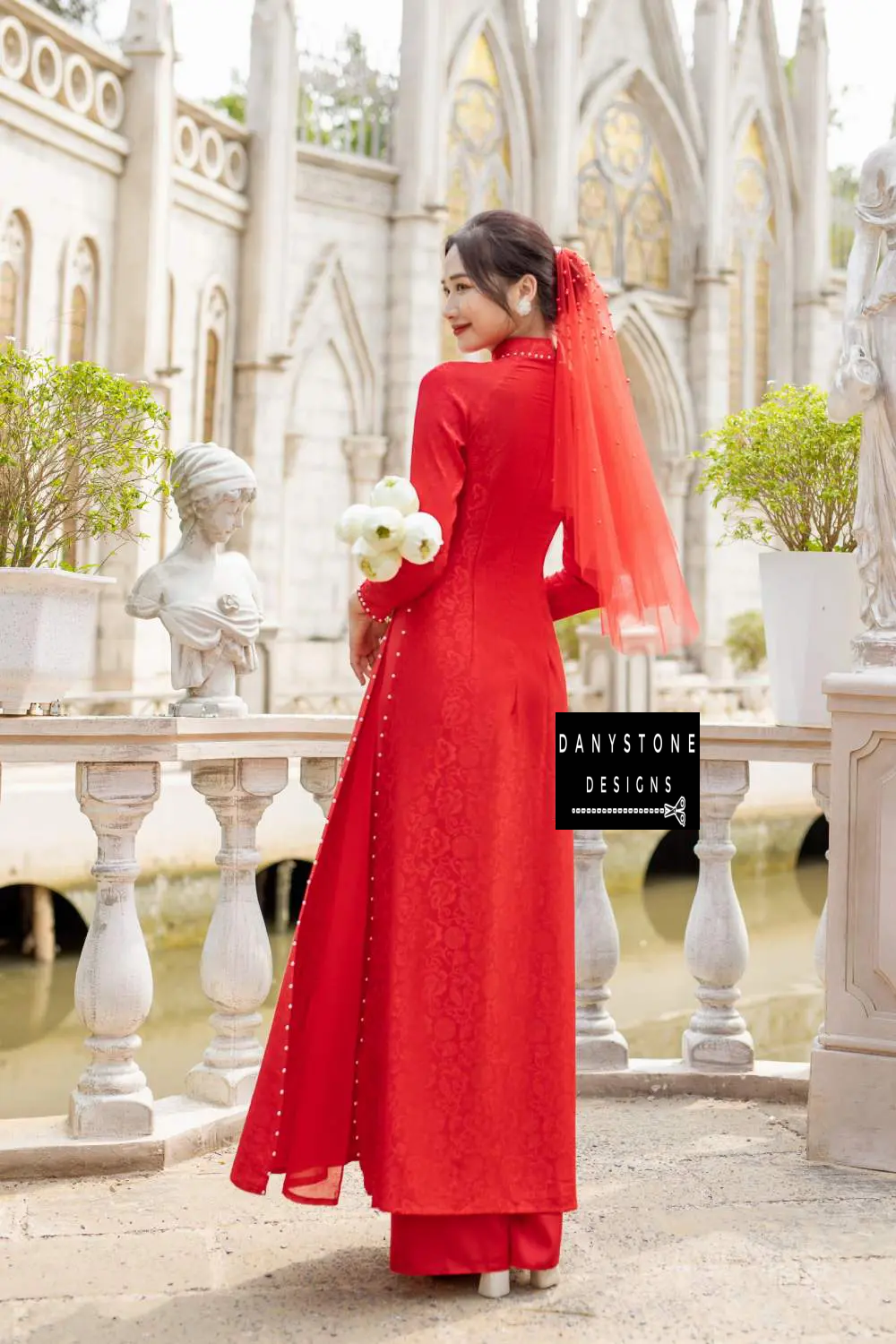 Close-up of the red brocade Áo Dài showcasing the intricate floral background and white pearl embellishments.