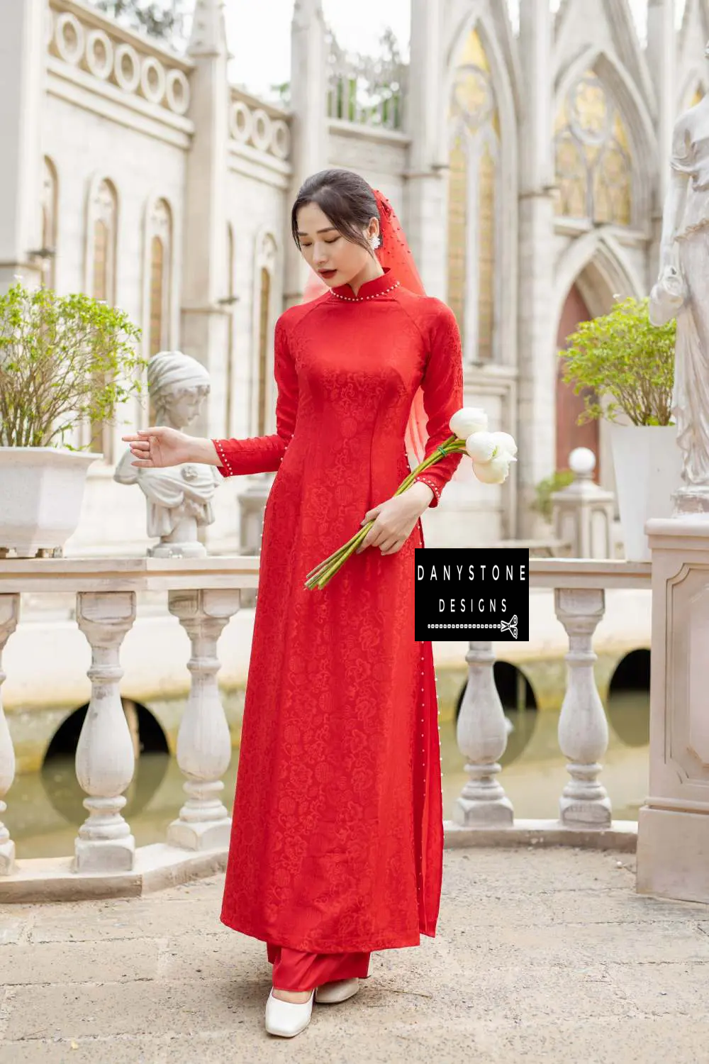 Side view of the red brocade Áo Dài highlighting the floral patterns and pearl-studded hem.
