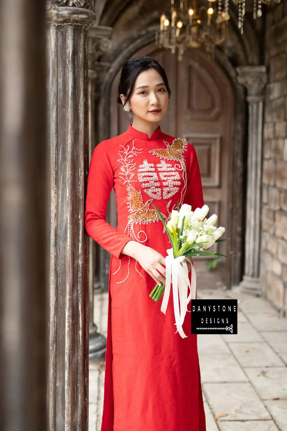 Full-length view of a bride in a red brocade Áo Dài with intricate phoenix details.