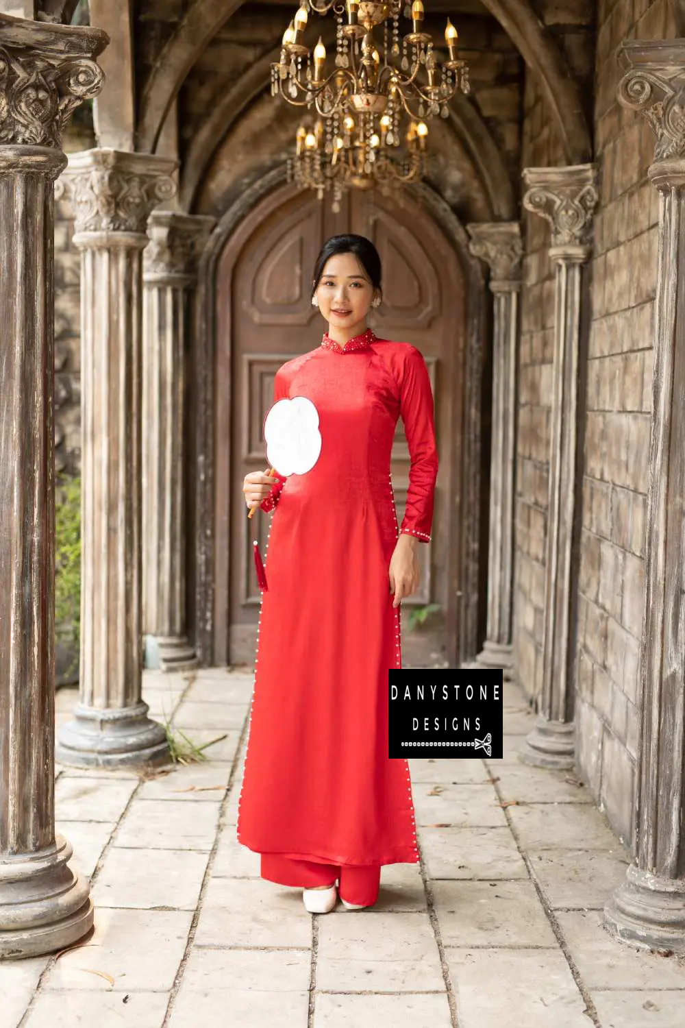 Elegant woman wearing a red brocade Áo Dài with beaded collar and pearl details.