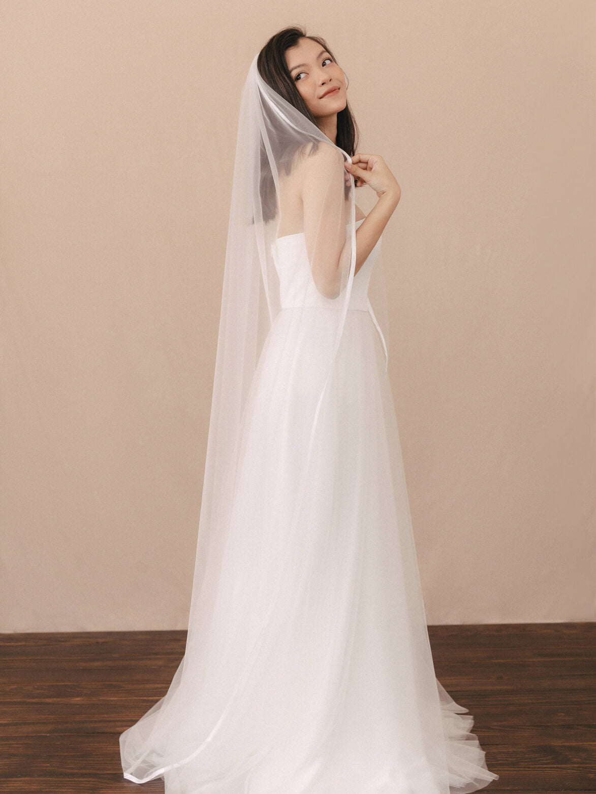 Woman wearing a white wedding dress with a veil against a beige background